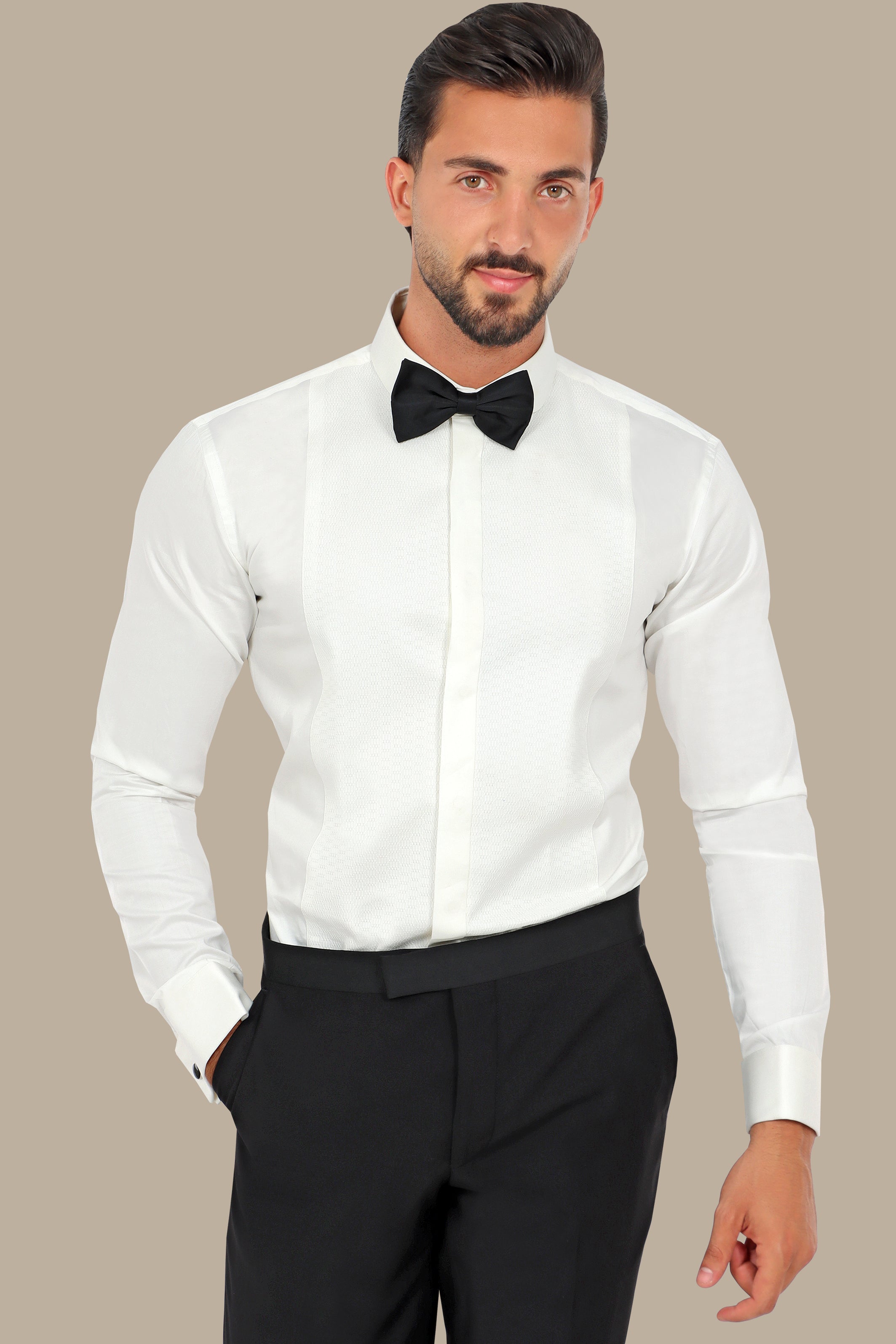 Man wearing a white dress shirt with a black bow tie and black pants against a beige background