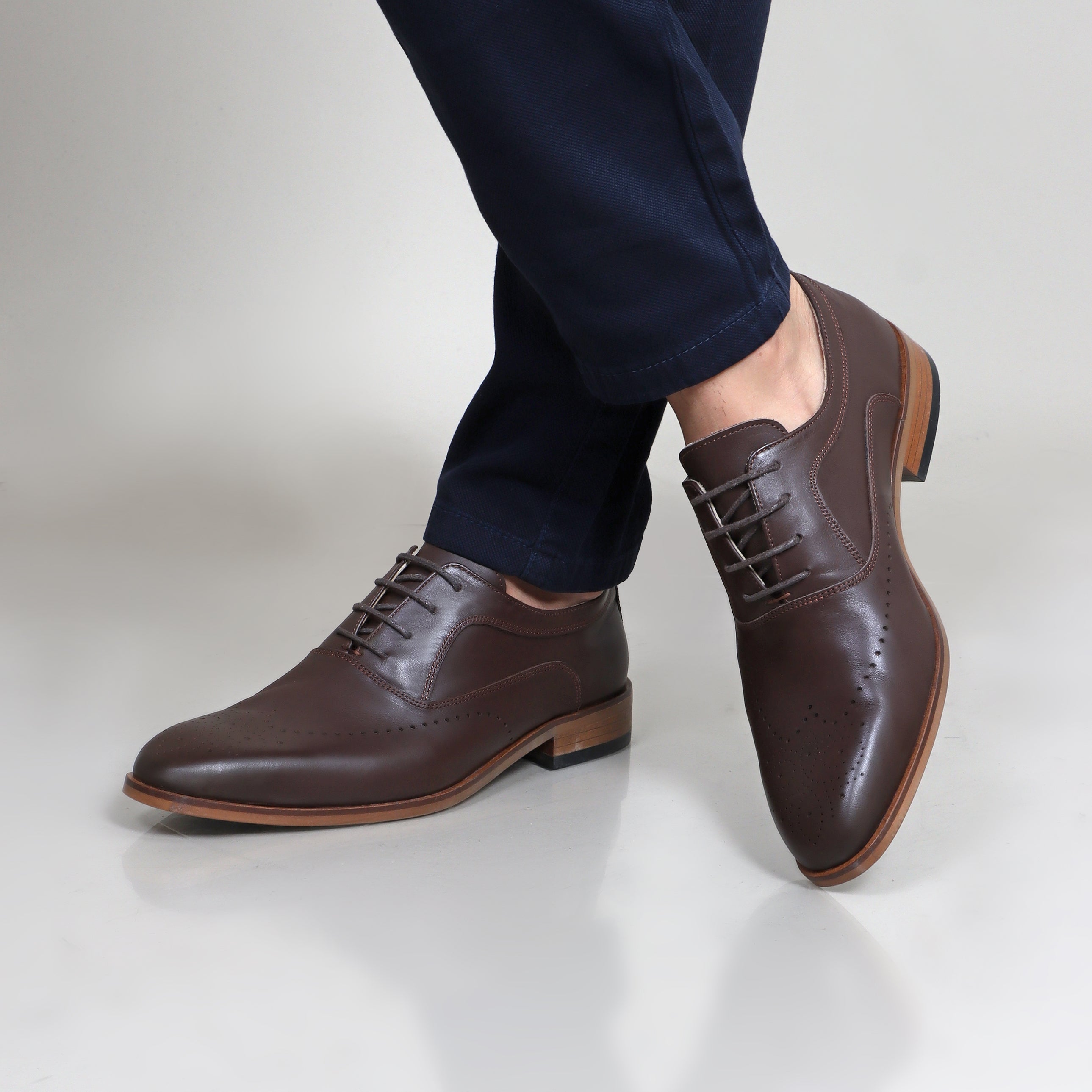Brown leather English classic shoes with lace-up design and wooden soles worn with navy pants.