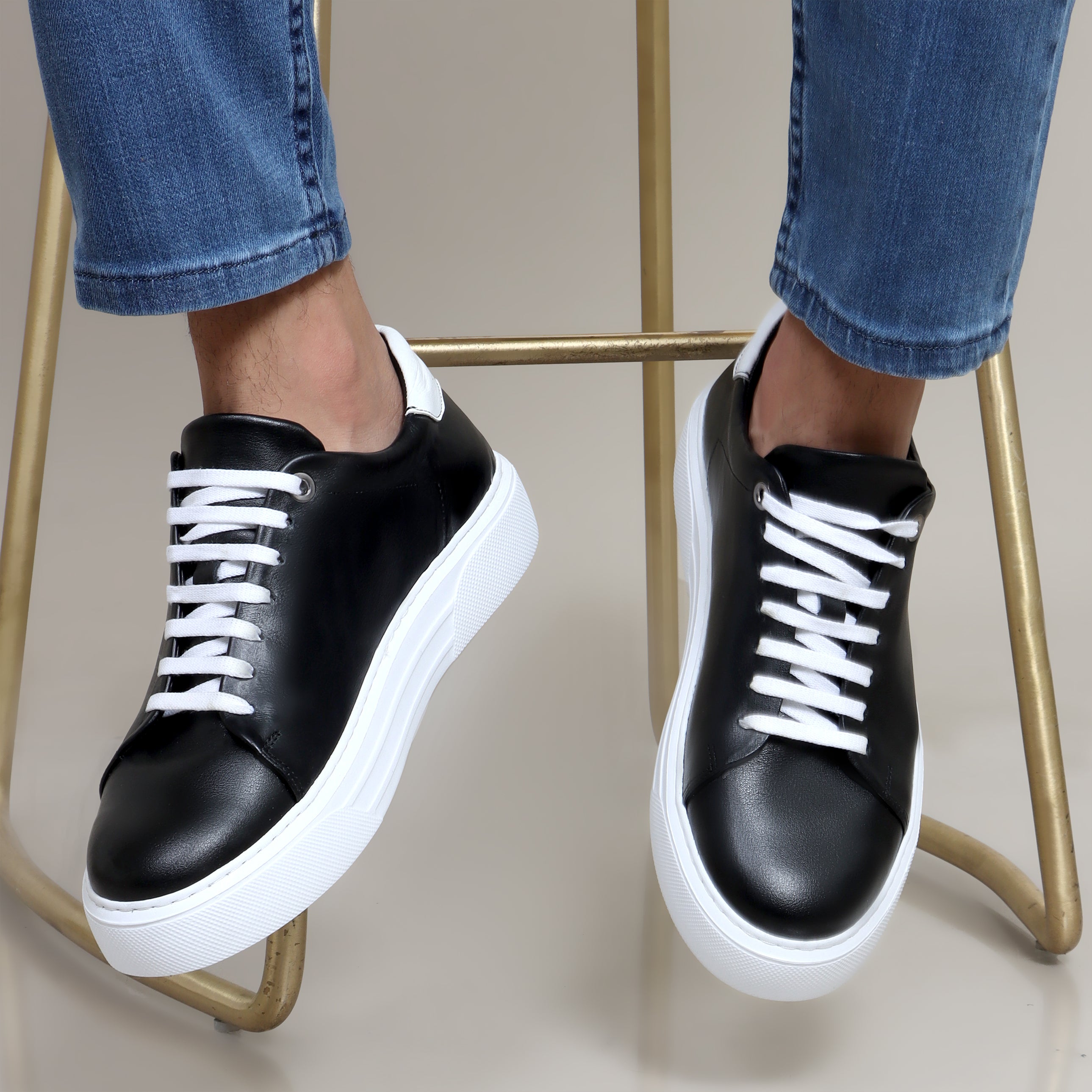 Black leather sneakers with white laces and thick white sole, white heel tab, worn with blue jeans.