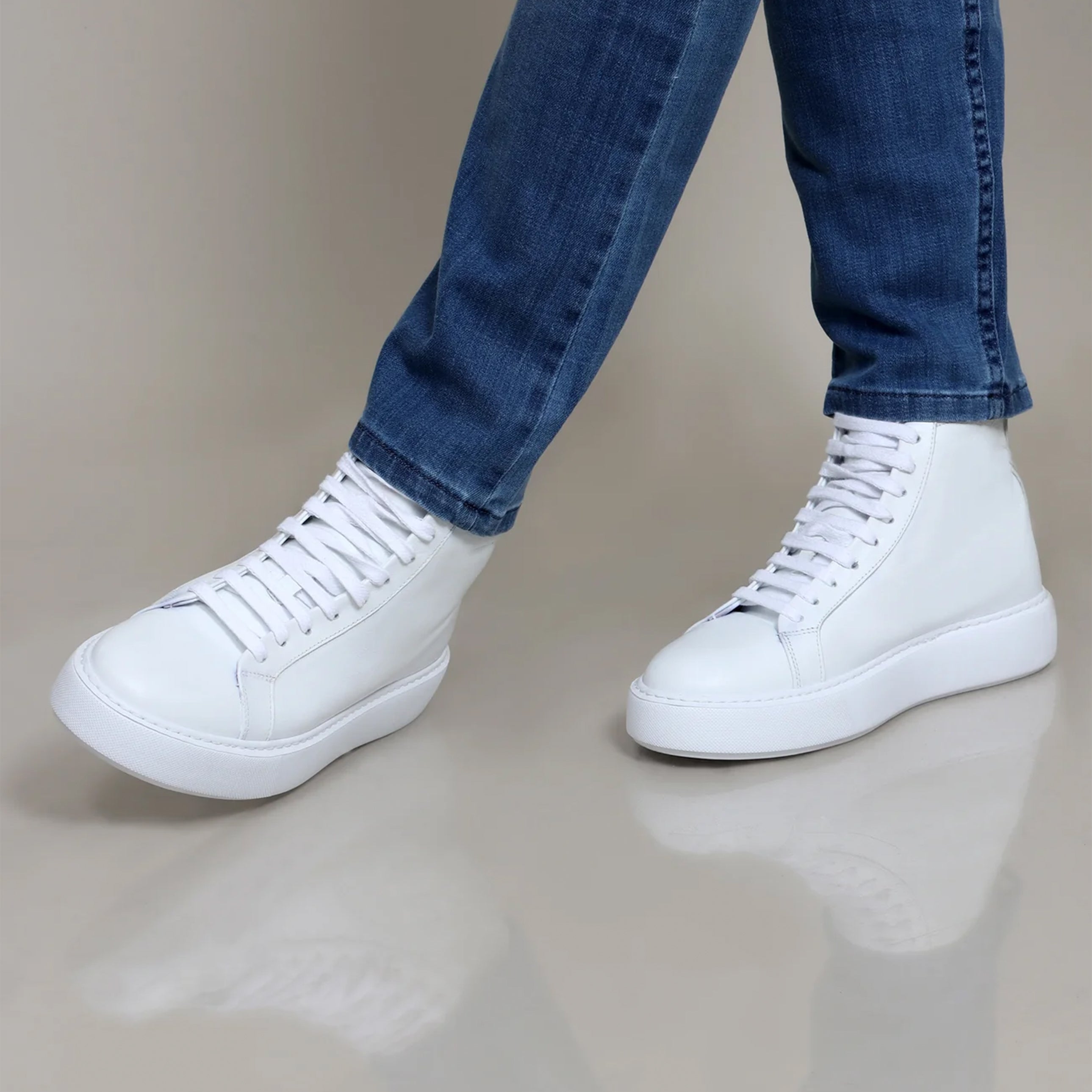 White high-top sneakers with thick soles and lace-up fronts, worn with blue jeans.