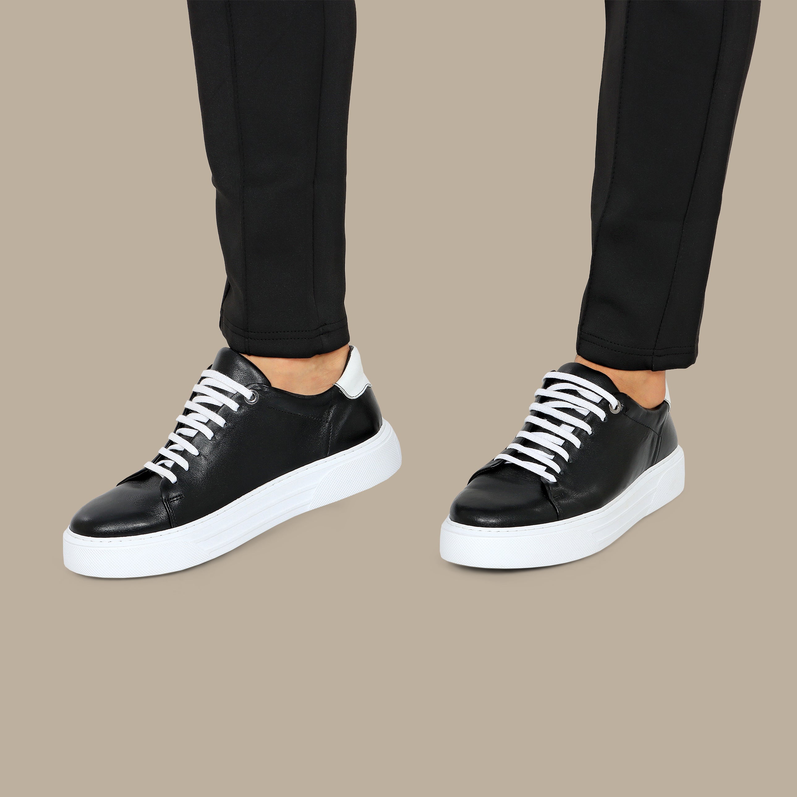 Black leather sneakers with white laces and thick white soles, featuring white heel accents.