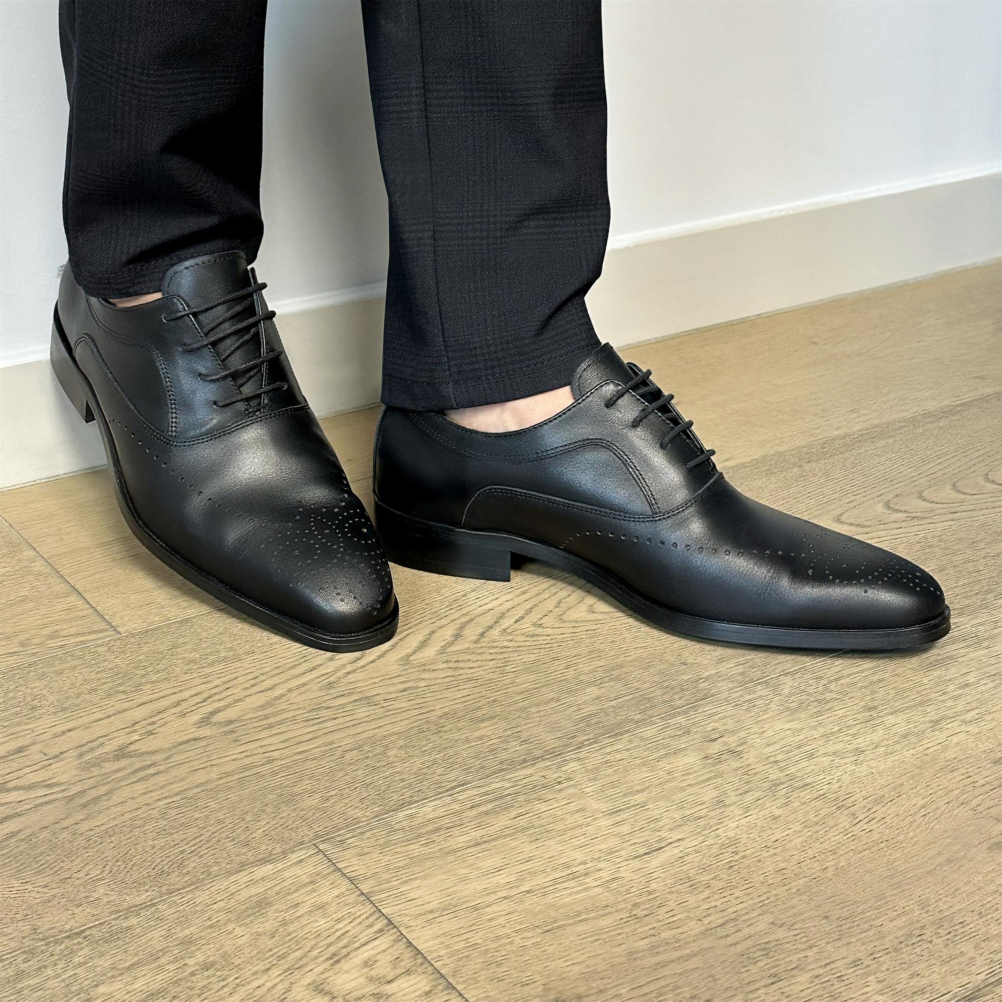 Black leather classic English dress shoes with pointed toes and thin laces on wooden floor.