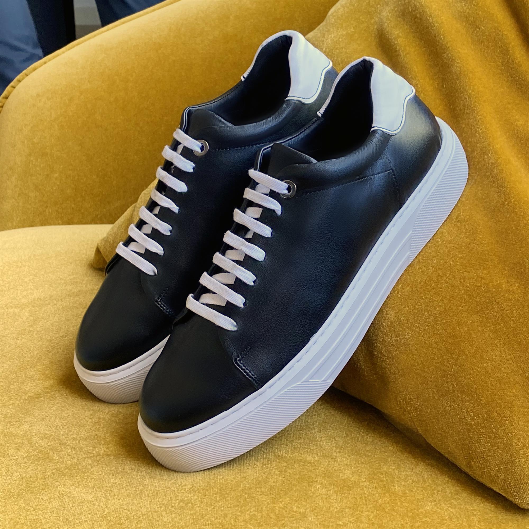 Black low-top sneakers with white heel tab and white rubber sole on a mustard fabric surface.